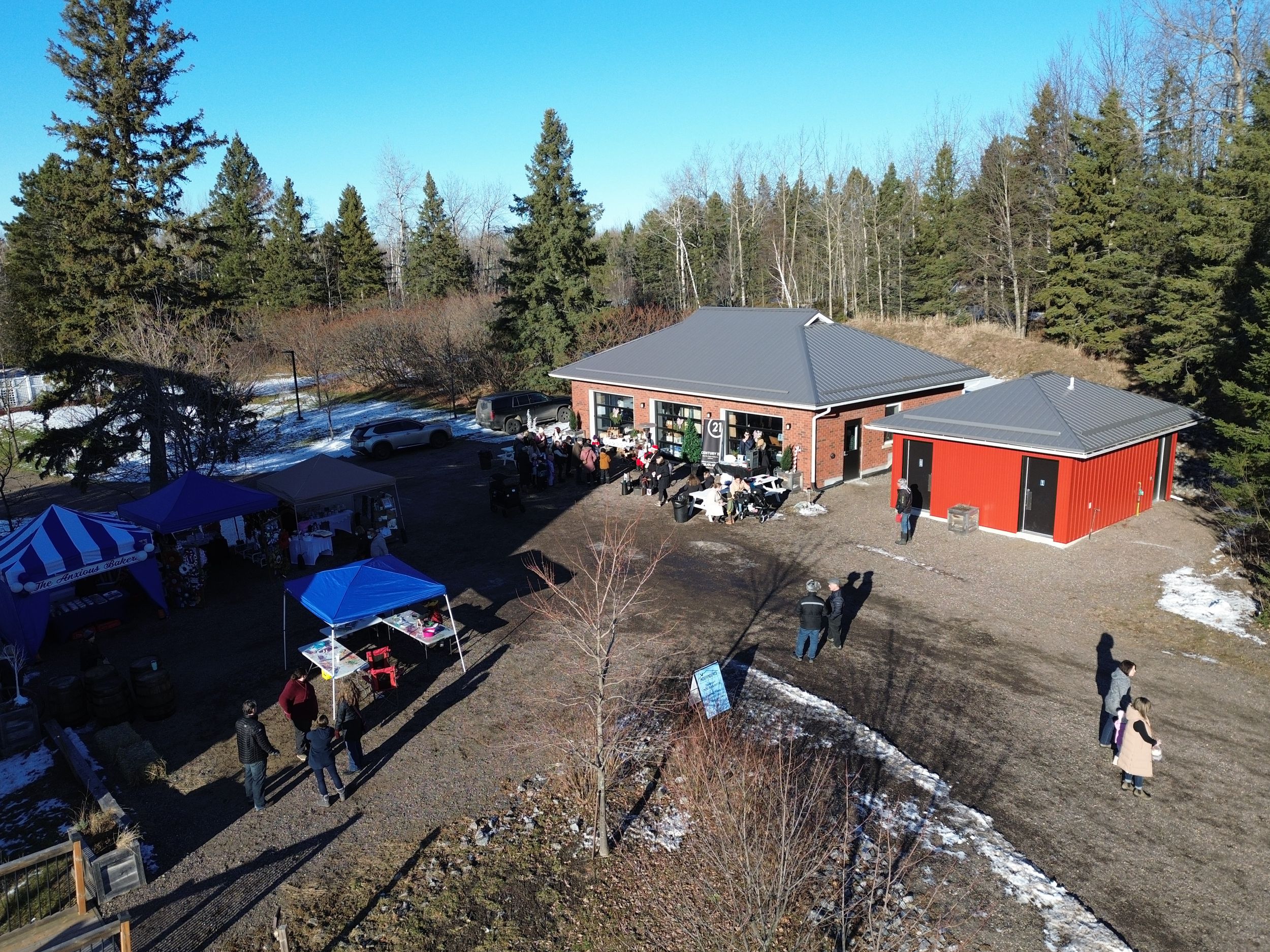 Aerial view of winter event at rural building with blue tents and parked cars.