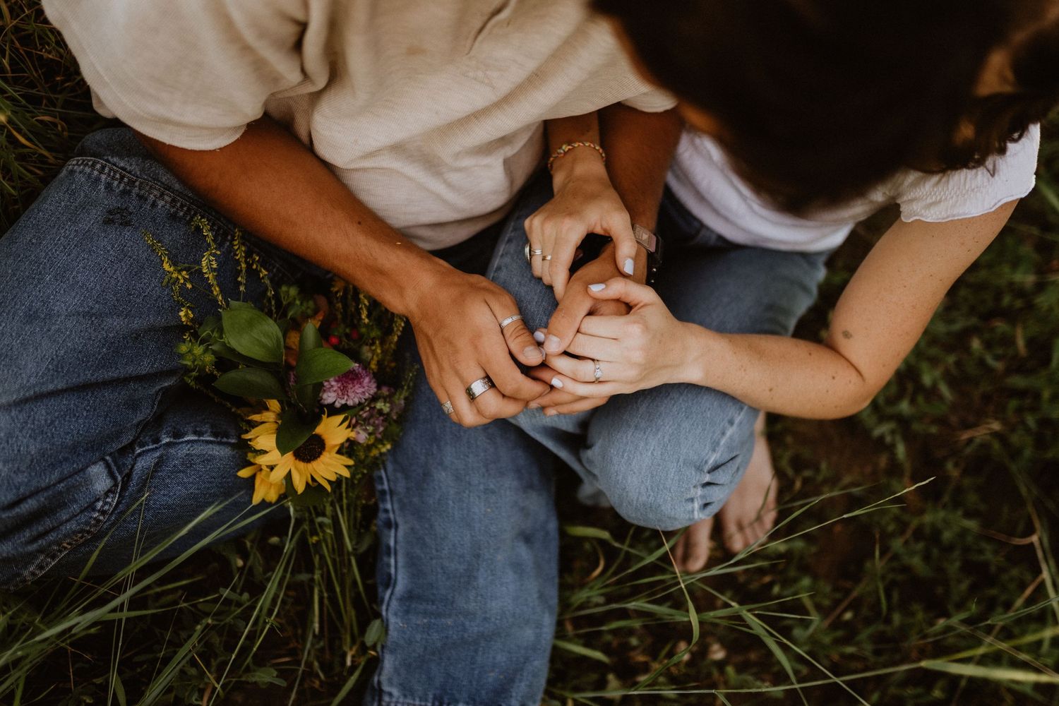 Close-up of hands holding sunflower against denim and grass background.