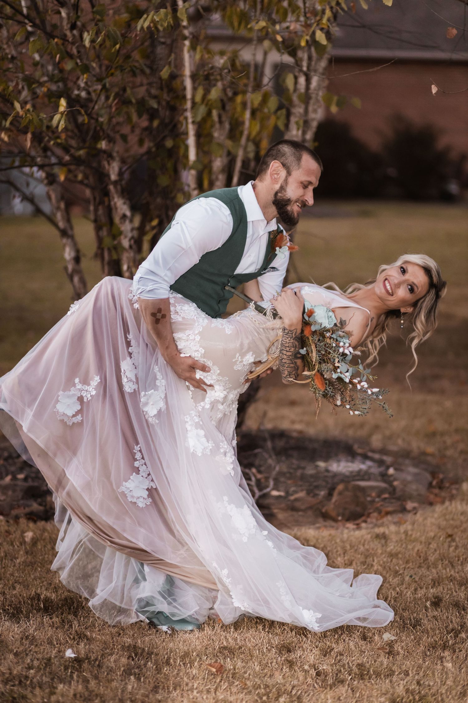 A groom in a green vest dips his bride in a romantic pose during their wedding photoshoot.