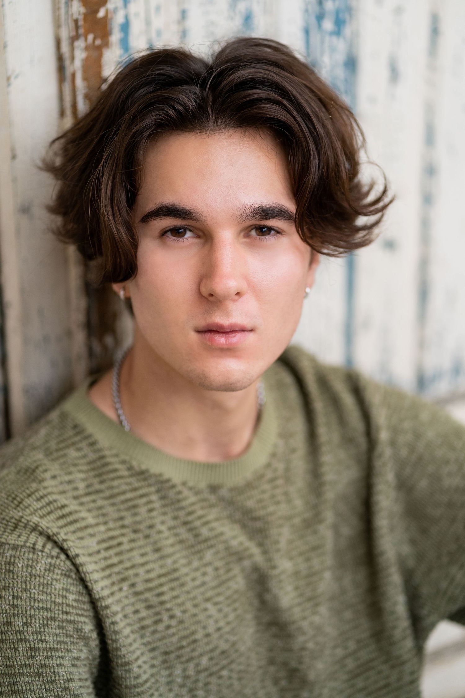 A high school senior in olive green sweater poses against textured wall in casual portrait.