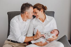 Familie teilt einen intimen Moment mit ihrem neugeborenen Baby auf einer grauen Couch.