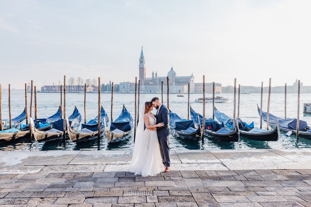 Hochzeitspaar posiert am Wasser von Venedig mit Kirche San Giorgio Maggiore und Gondeln im Hintergrund.