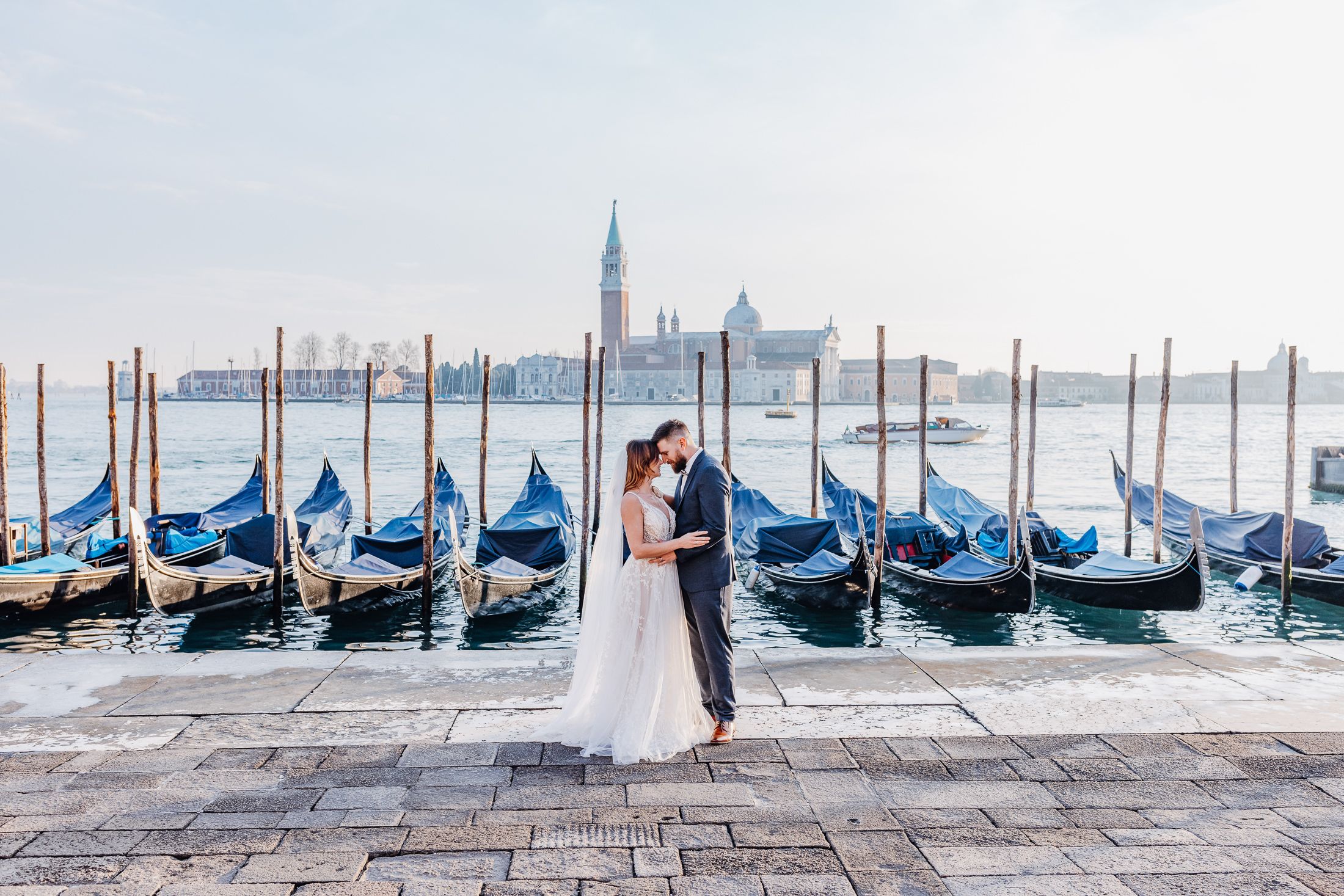 Hochzeitspaar posiert am Wasser von Venedig mit Kirche San Giorgio Maggiore und Gondeln im Hintergrund.