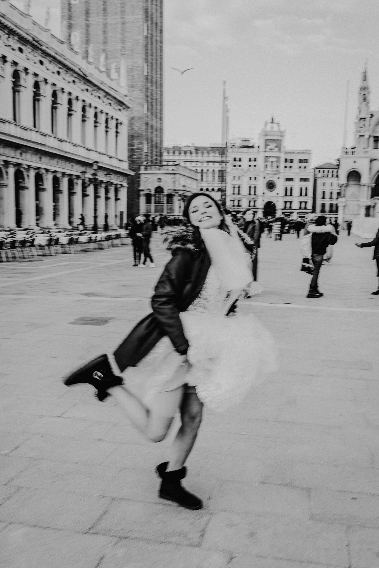 Fröhliche Person tanzt in schwarz-weißem Kleid auf dem Markusplatz in Venedig.