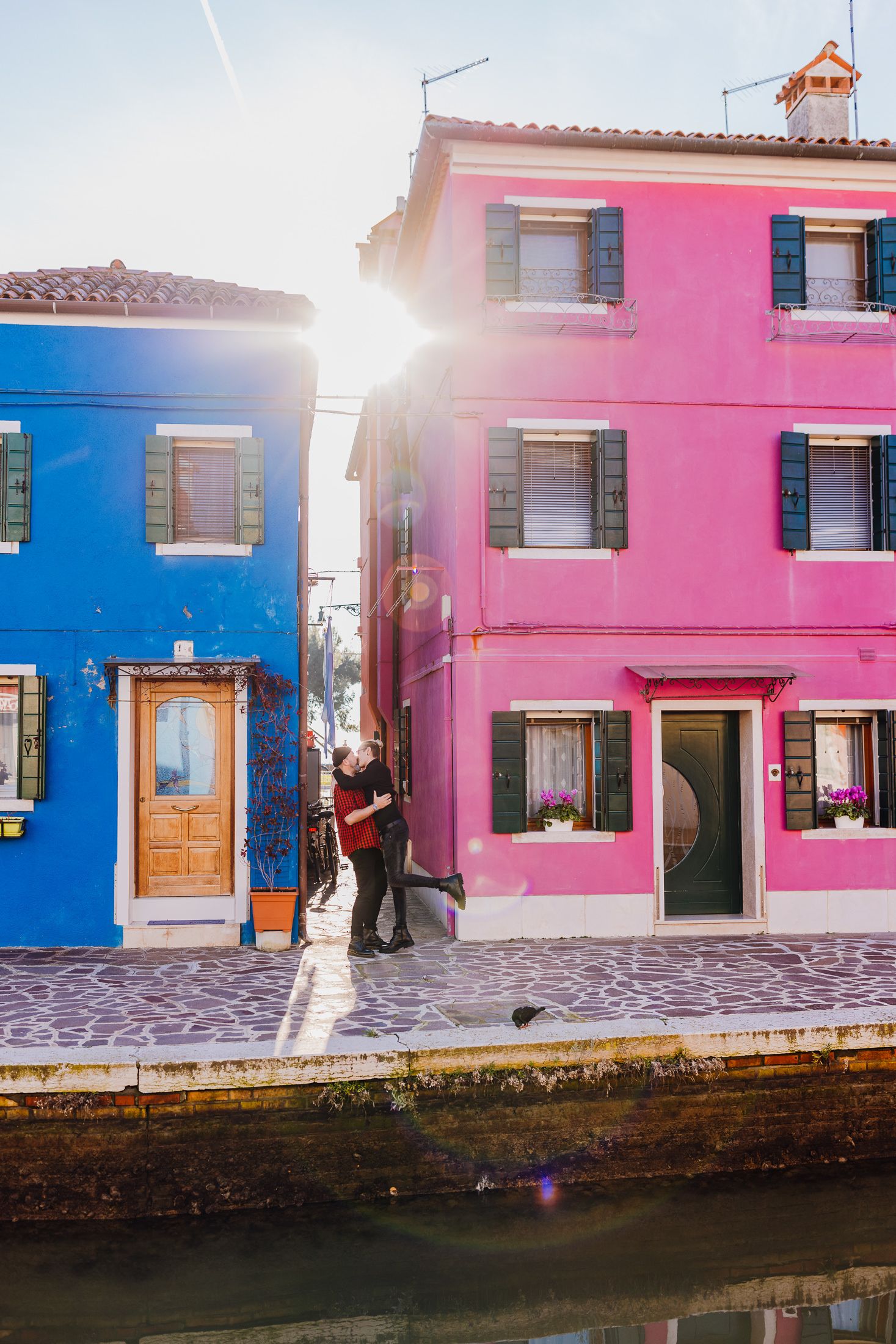 Lebendige rosa und blaue Häuser entlang des Kanals in Burano, Italien, mit durchströmendem Sonnenlicht.
