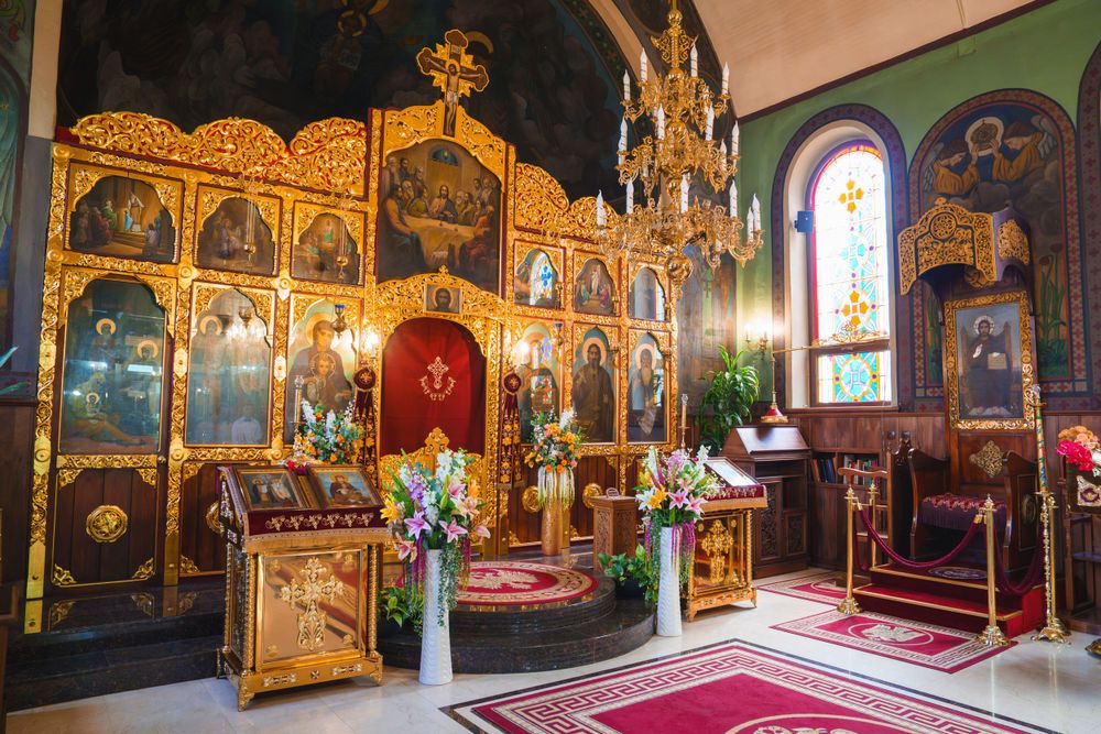 Orthodox church interior featuring a golden iconostasis with religious artwork and red carpet runners.