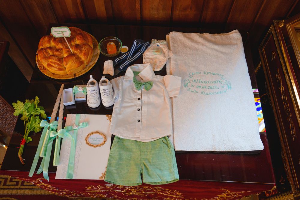 Baptismal clothing and accessories arranged on a wooden surface with traditional bread.
