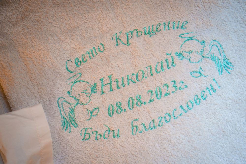 Embroidered baptismal text in mint green on a soft white textile surface.