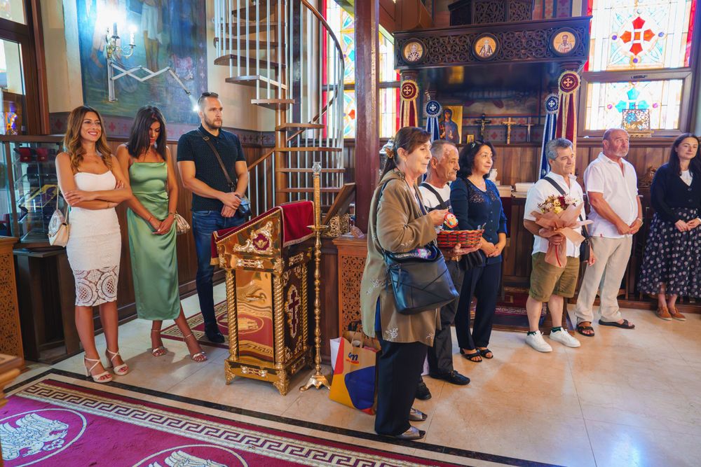 Group of attendees standing during a religious ceremony inside an ornate church with stained glass windows.