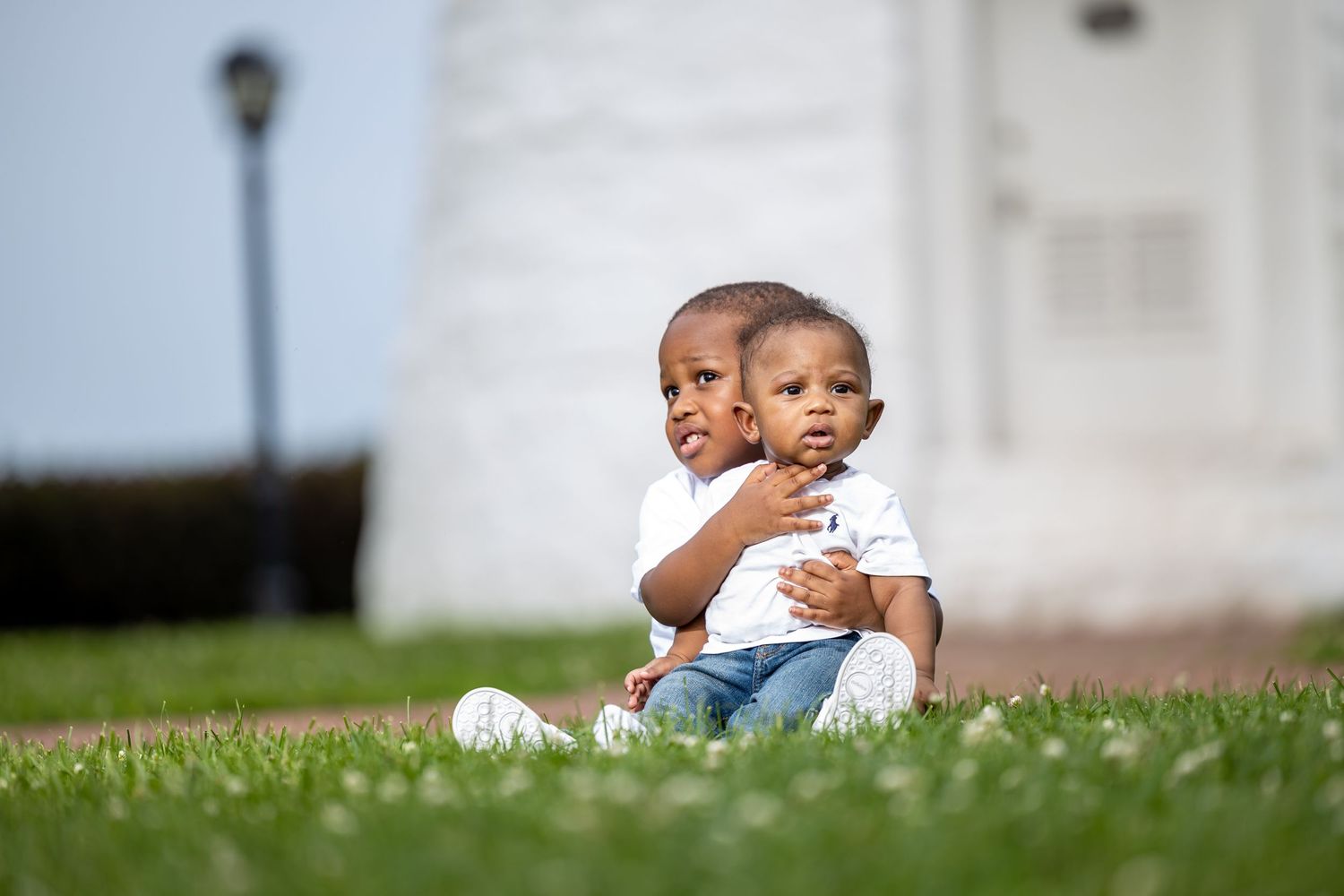 Children sitting together on grass with lighthouse in background.