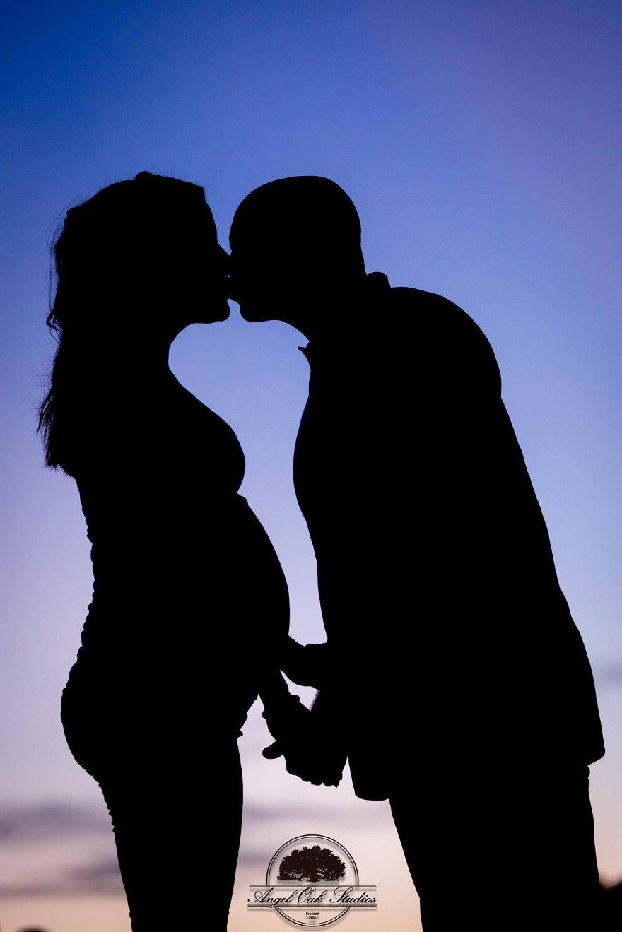 Pregnant couple silhouette kissing at sunset