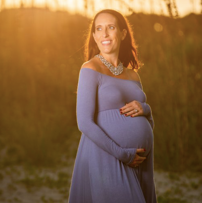 Pregnant mom embraces baby bump on the beach with seagrass backdrop