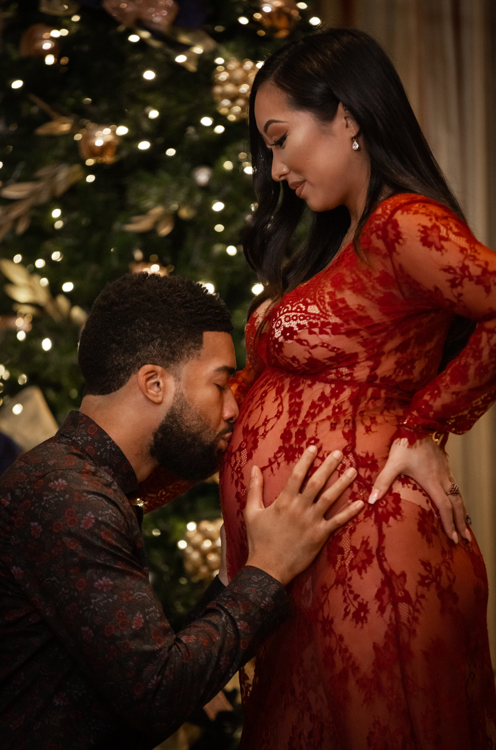 Daddy kissing baby bump in front of Christmas tree