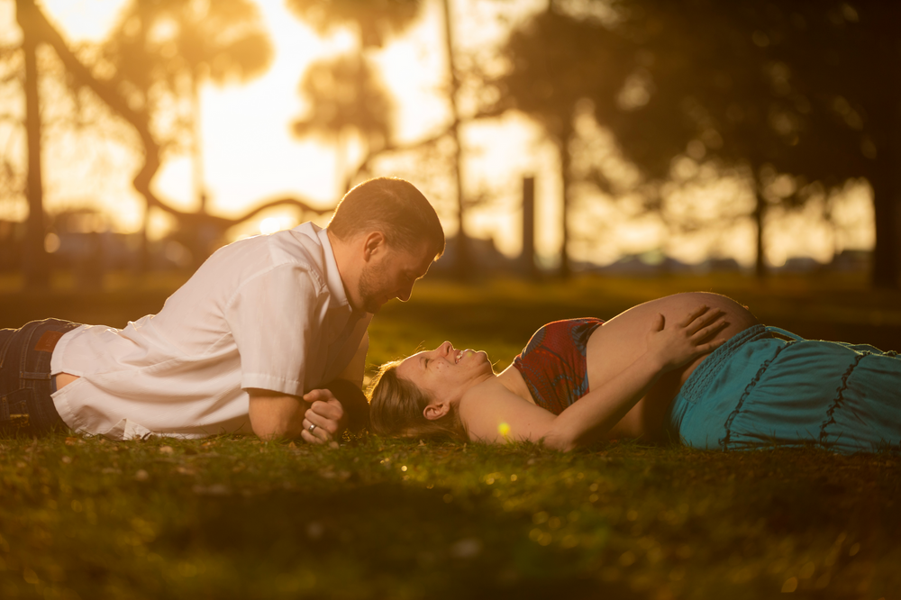 Pregnant couple lay on the ground in park