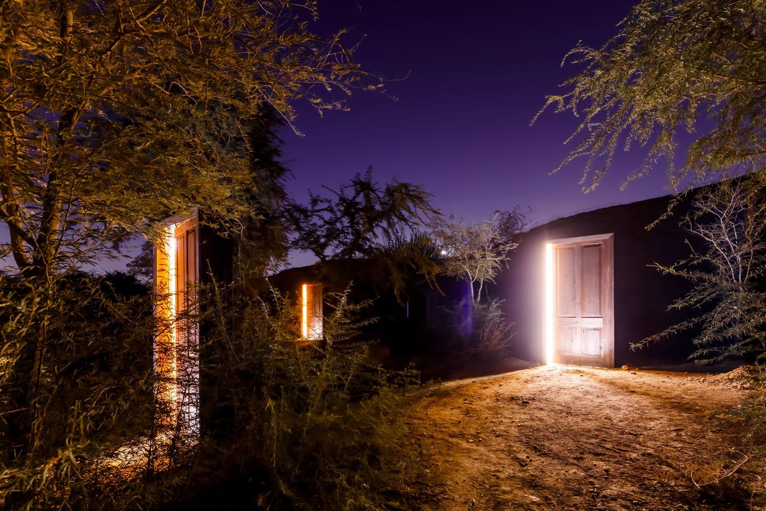 Illuminated doorways stand mysteriously in nature against purple night sky with trees.