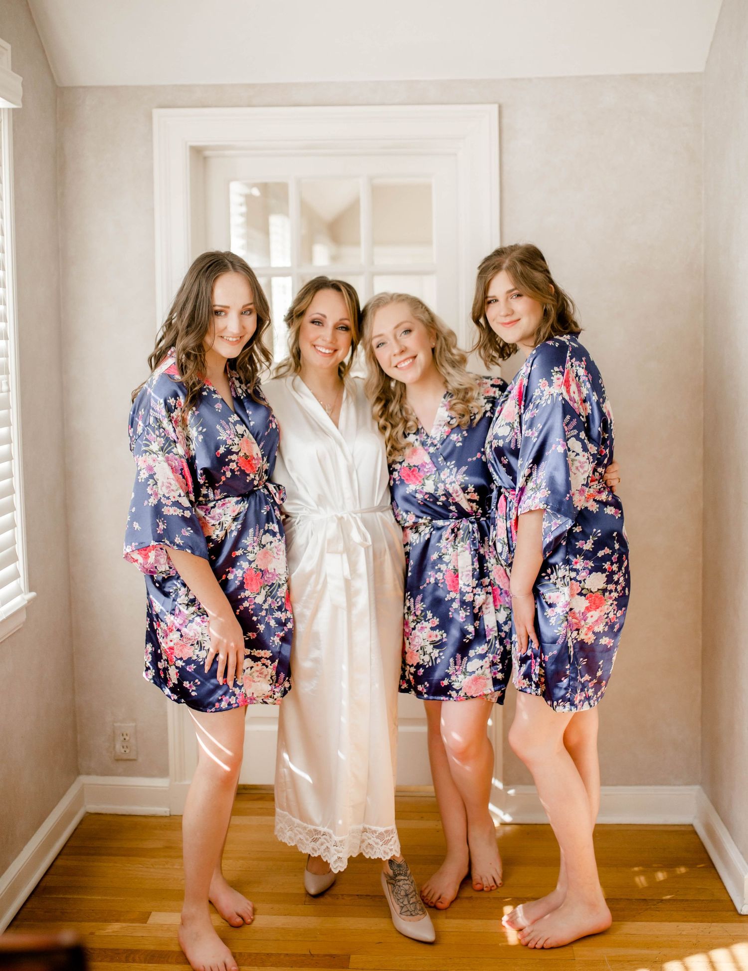 Wedding party poses in matching floral robes while getting ready in a sunny room.