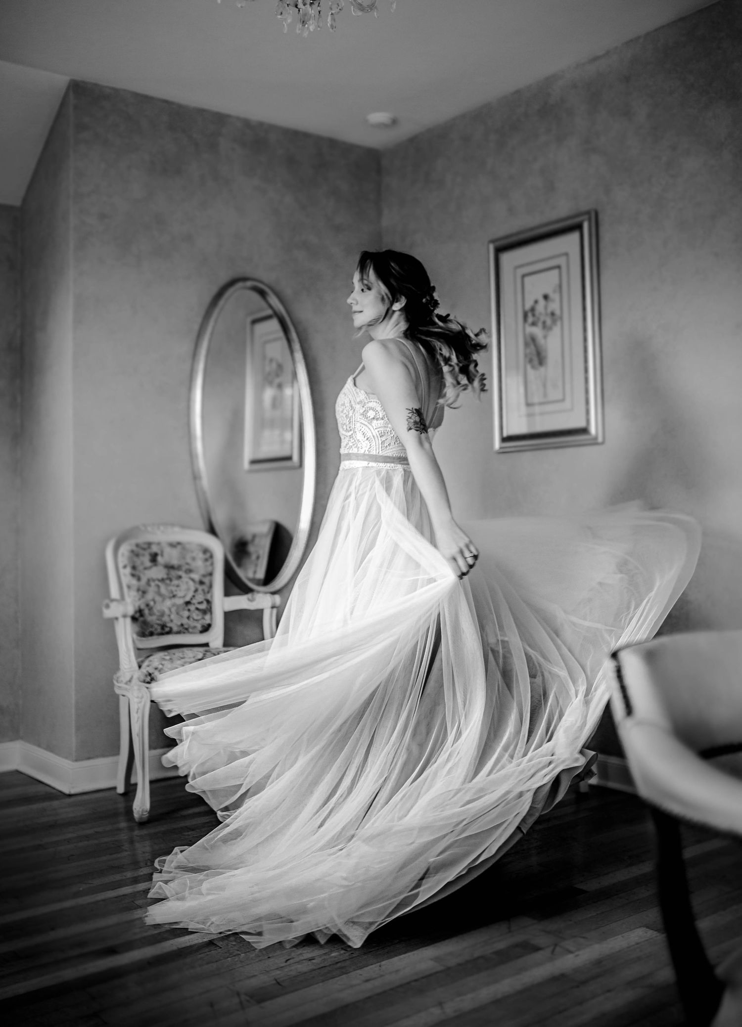 A flowing white wedding dress twirls elegantly in a room with a vintage mirror and chair.
