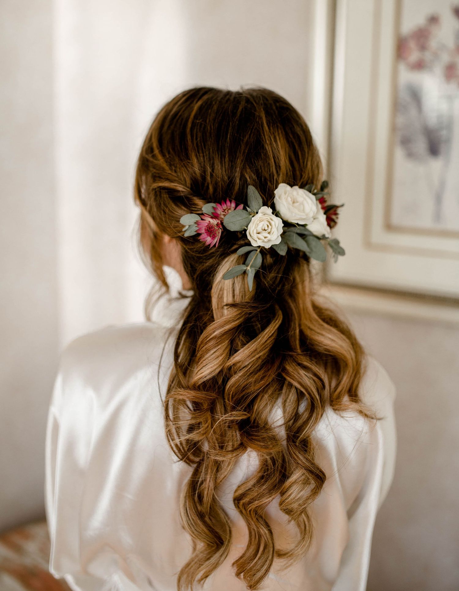 Romantic bridal hairstyle with soft curls adorned with pink and white floral accessories.