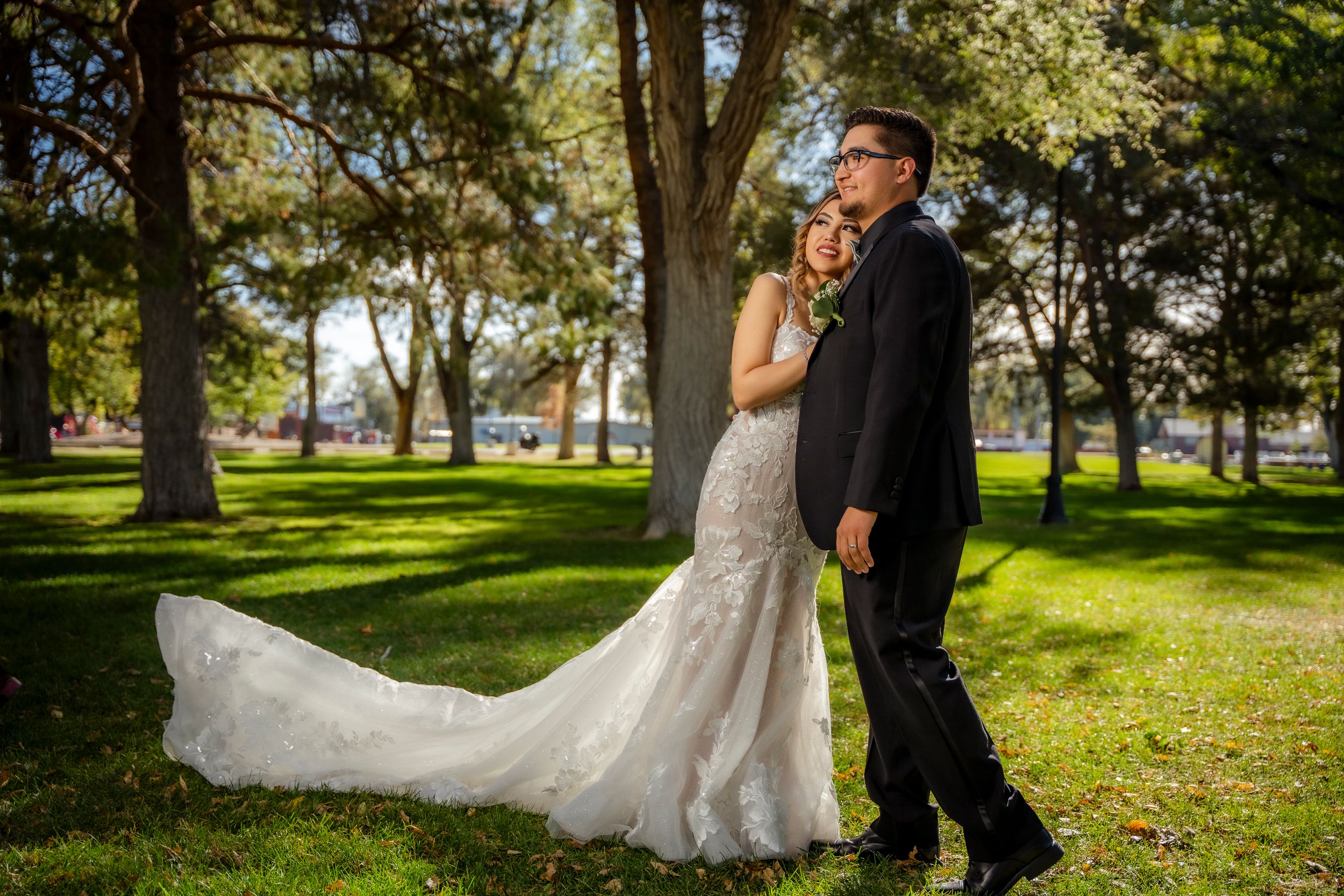 Bride and groom share romantic moment in park, bride wearing lace mermaid gown with long train.