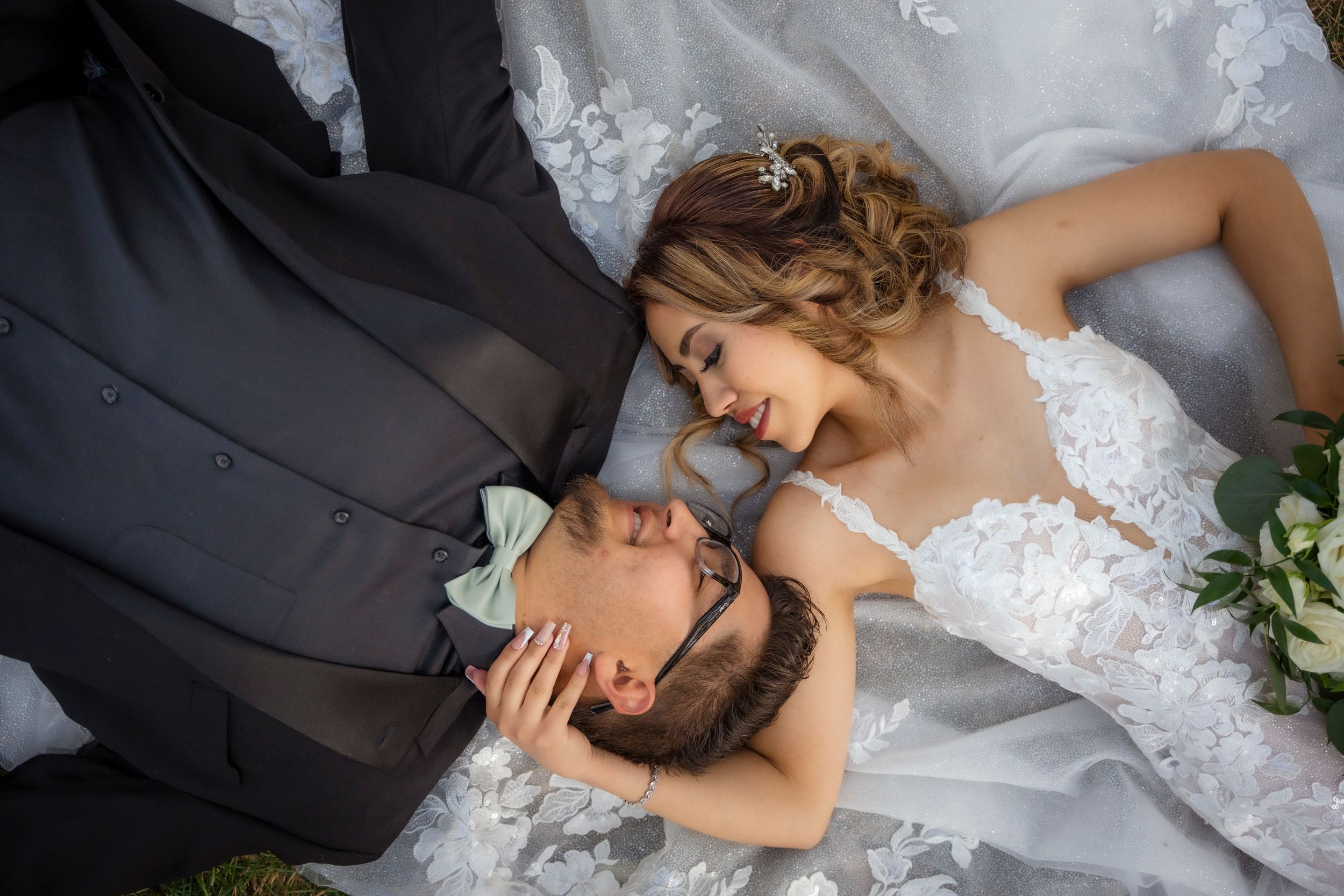Bride and groom lie on wedding dress train in intimate overhead romantic wedding portrait.