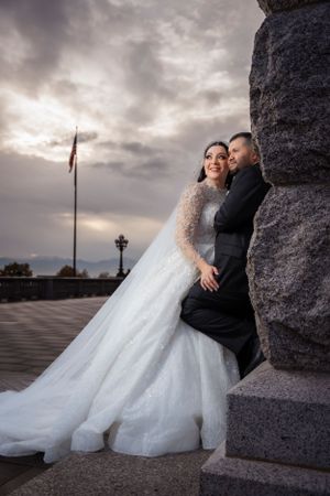 Bride and groom pose romantically against stone monument in sparkly ball gown at sunset wedding photo.