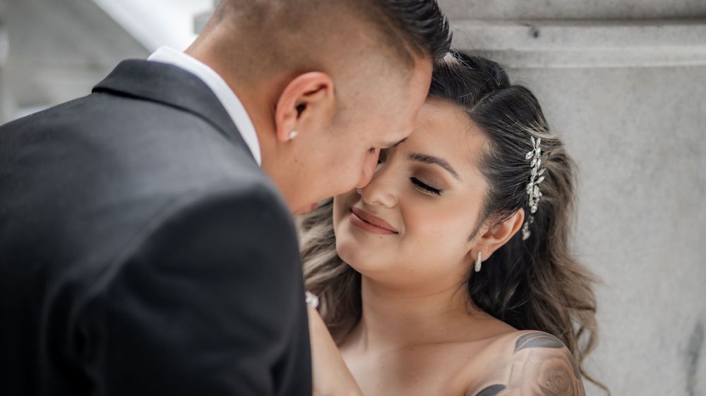 Groom tenderly kisses bride on forehead as she smiles wearing hair accessory in close portrait.