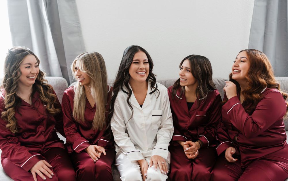 Group of bridesmaids in burgundy robes lounging and laughing together.