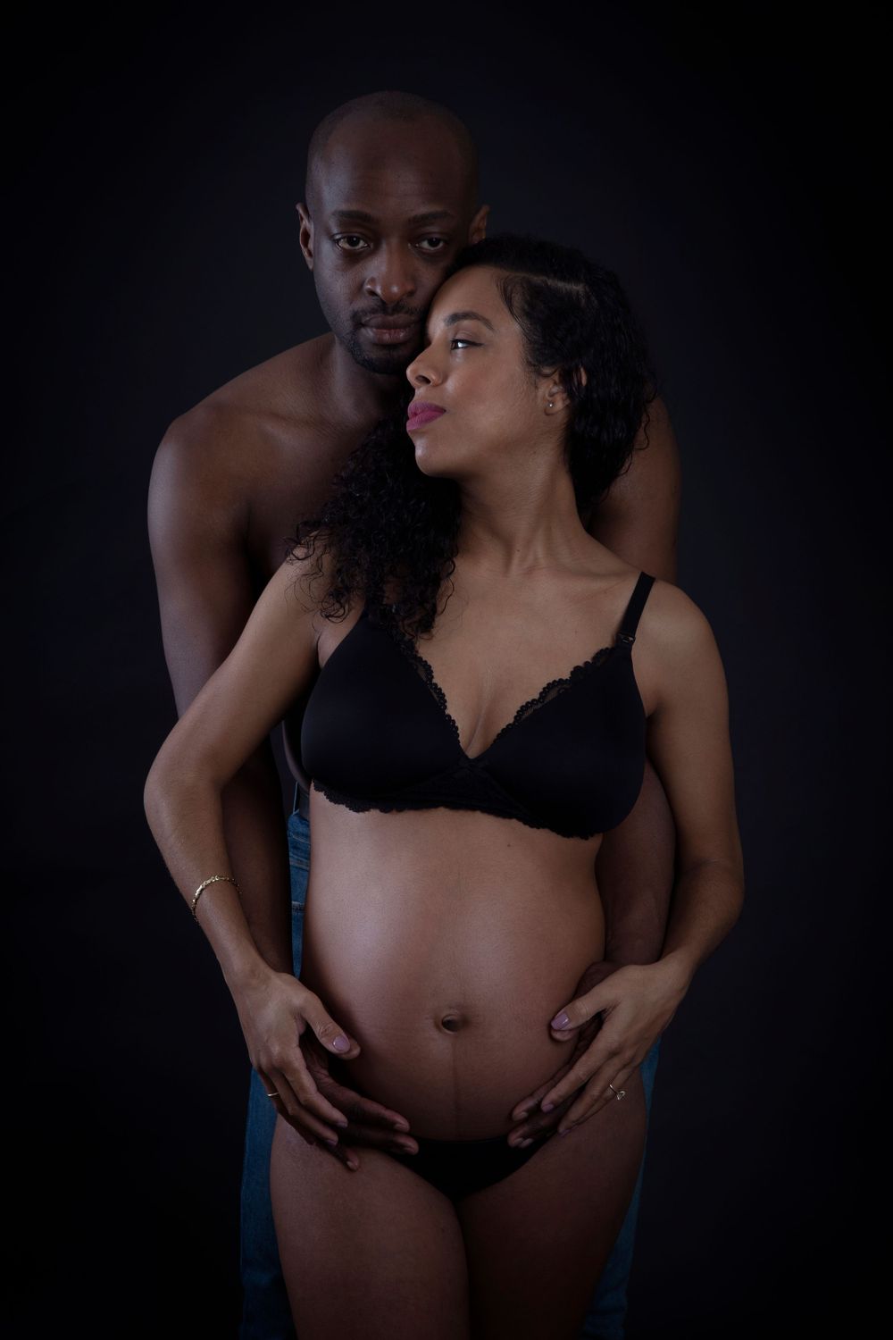 Intimate maternity photograph of couple in dark studio setting.
