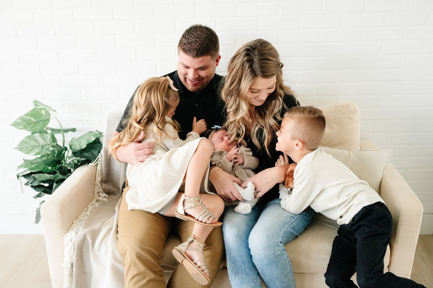 Family lounging together on white couch with house plant in background.
