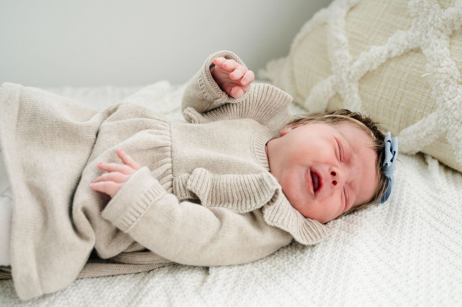 Newborn baby in beige sweater sleeping on white blanket.