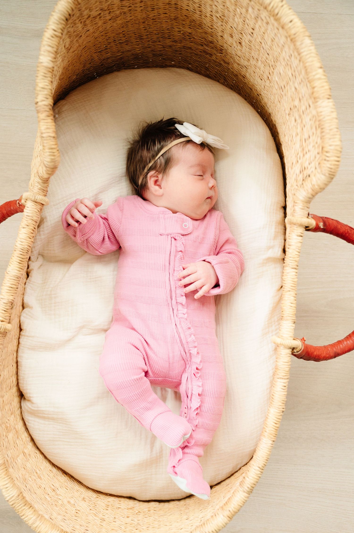Sleeping newborn in pink onesie lying in Moses basket.