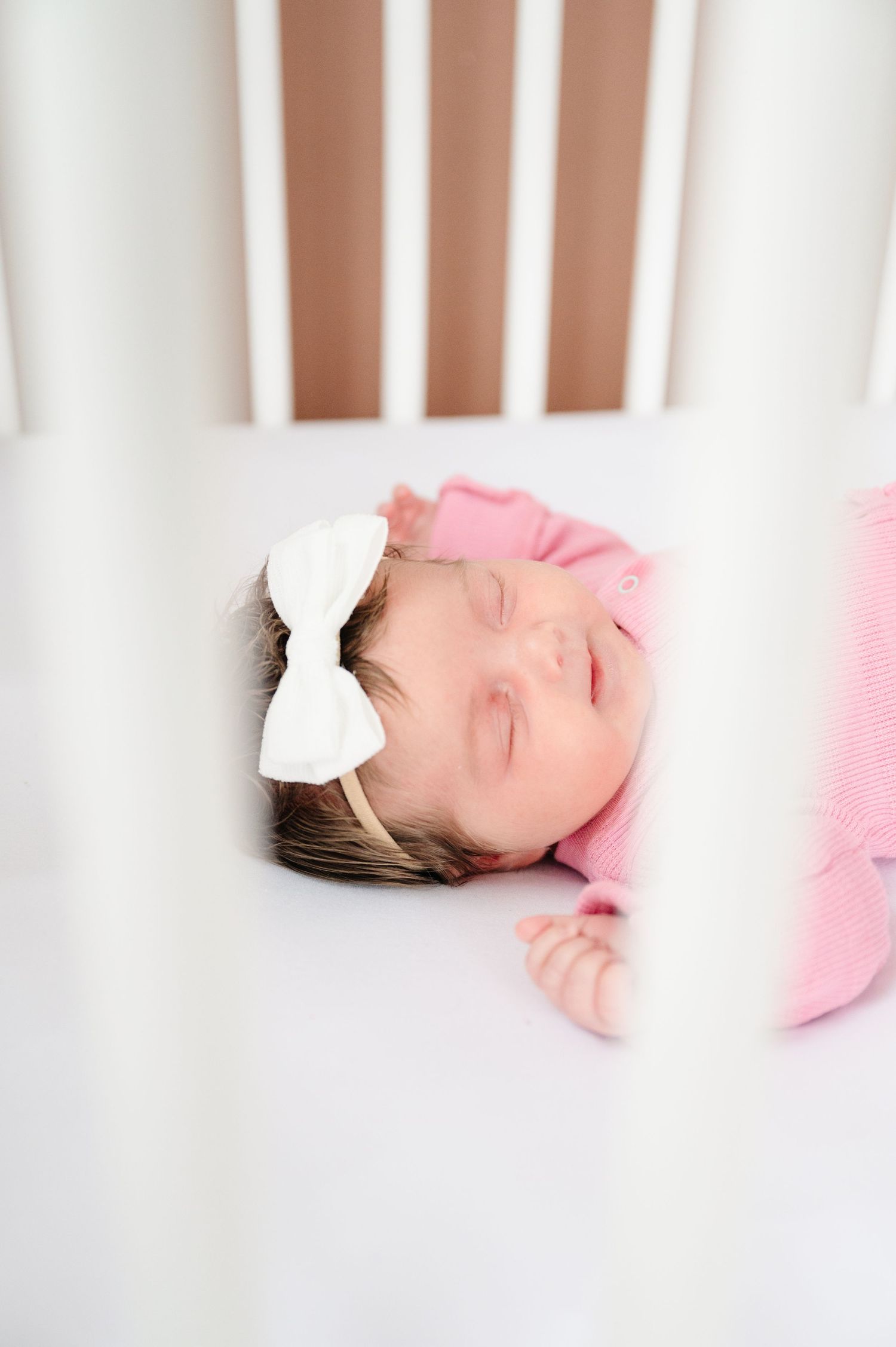 Sleeping baby with white bow headband in crib.