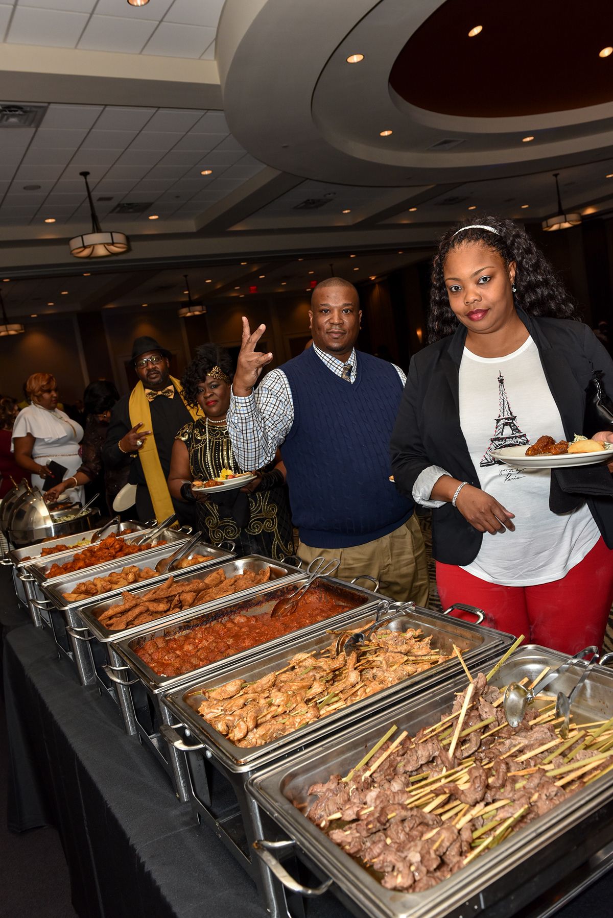 Guests standing by buffet line with chafing dishes full of catered food at formal event.