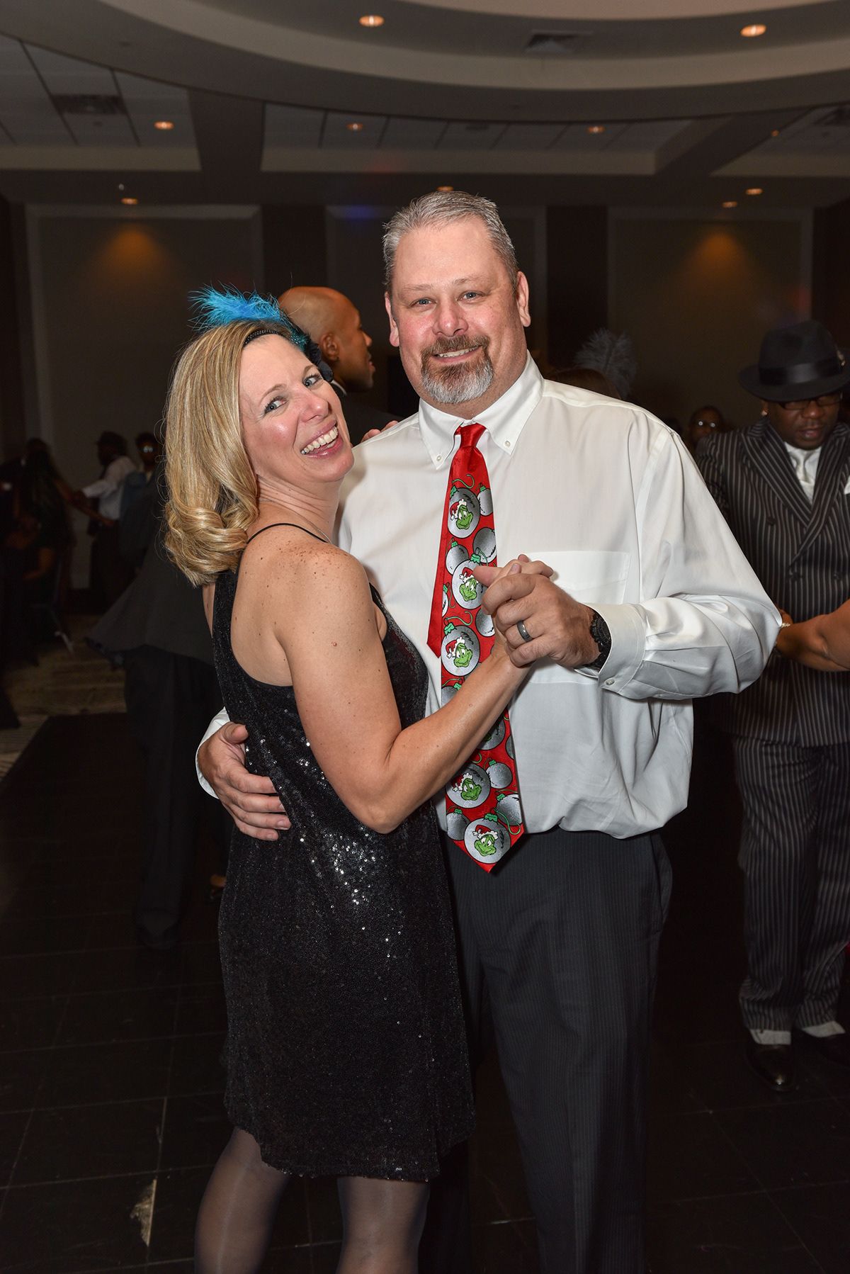 Couple dancing together at formal event, woman in sparkly black dress and man wearing festive tie.