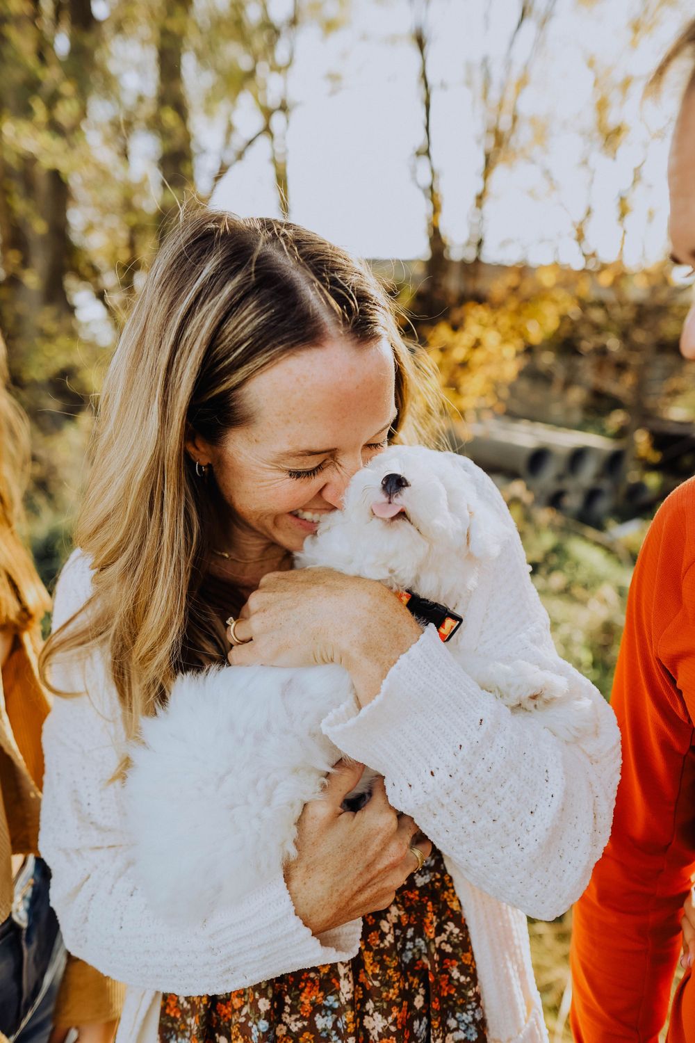 White fluffy dog receiving affectionate kisses in warm autumn sunlight.