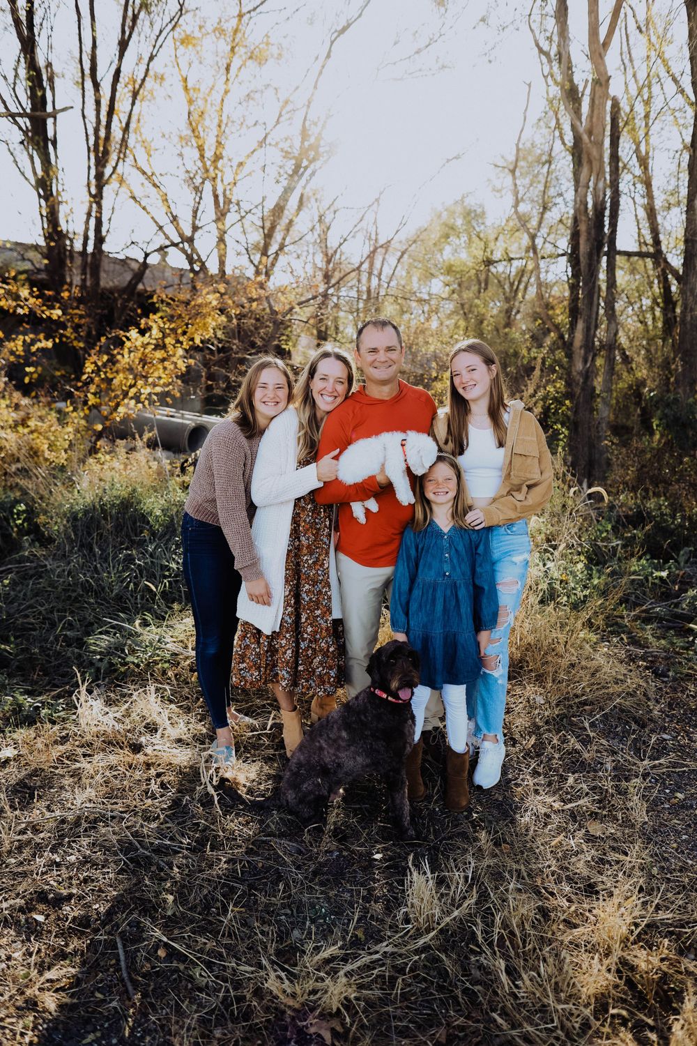 A group poses together with their dogs on a fall day in the woods.