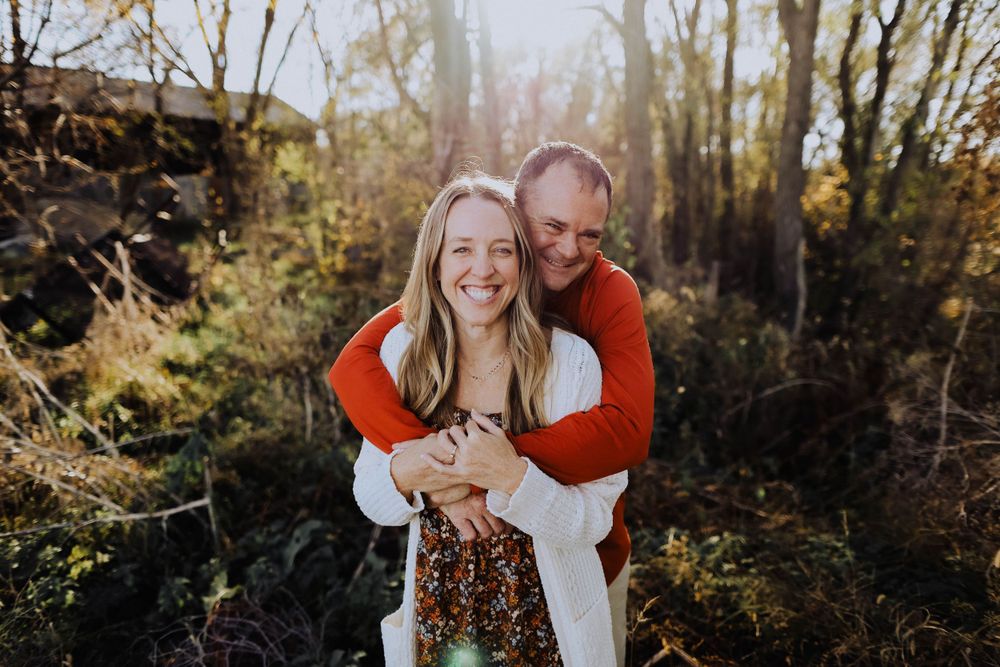 A couple shares a playful embrace in a sunlit forest setting.