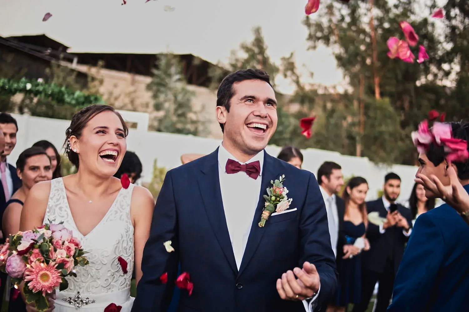 Joyful wedding ceremony exit with guests throwing pink flower petals at the newlyweds.