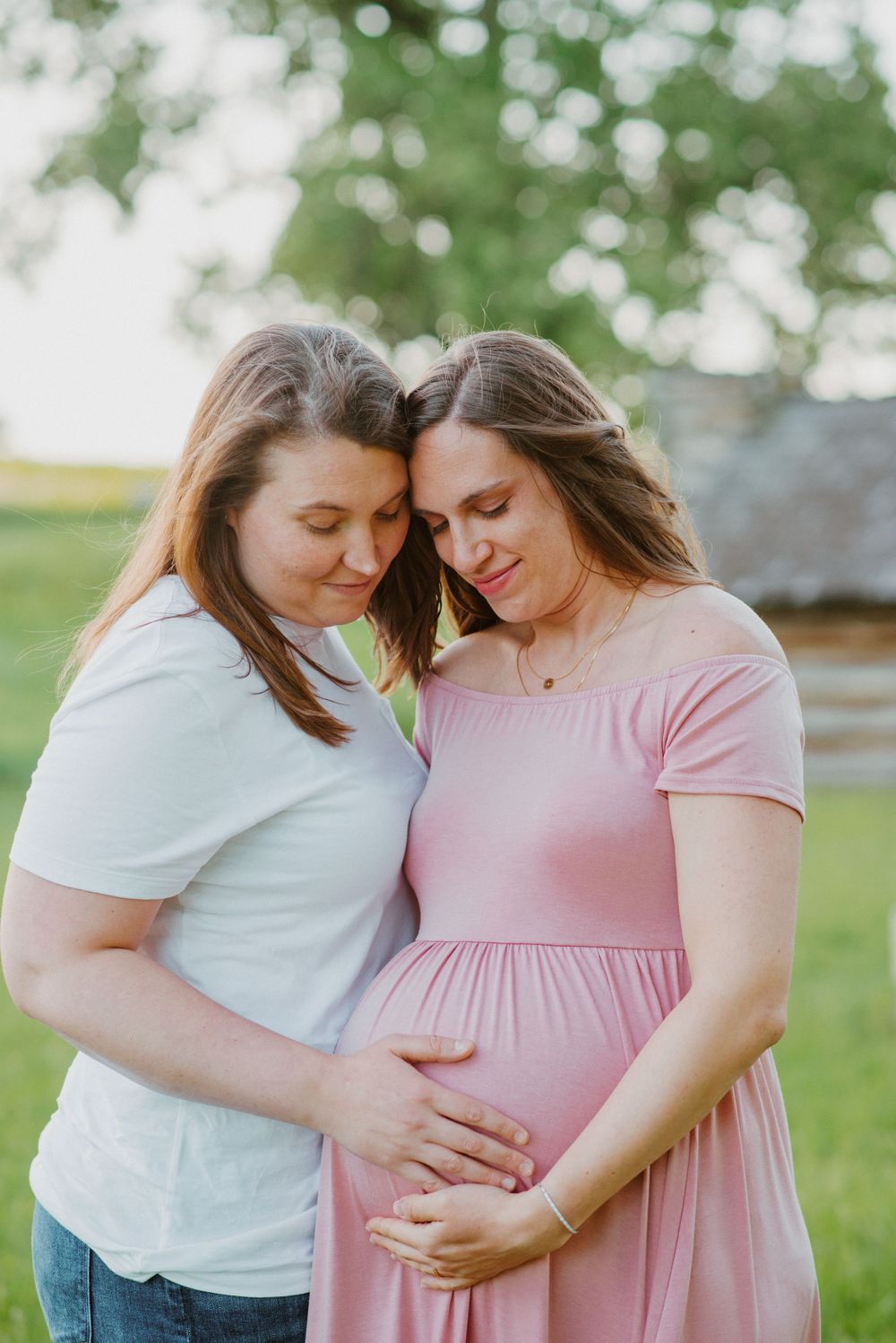 Two moms looking down at baby hand on tummy during maternity session