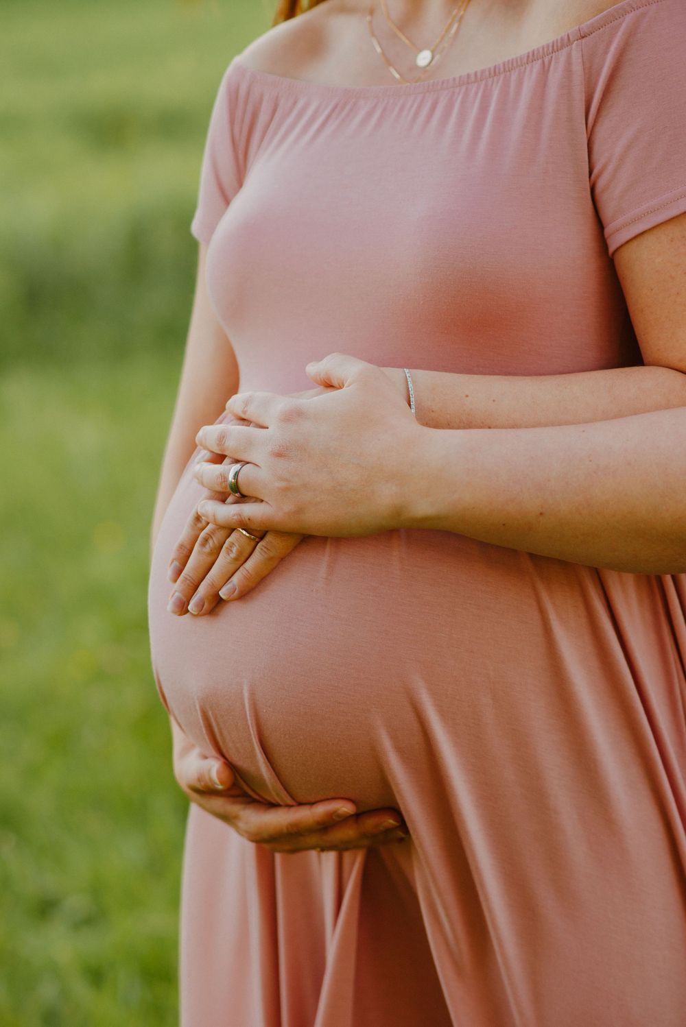Mom to be and partner with hands over tummy wearing pink dress during maternity session
