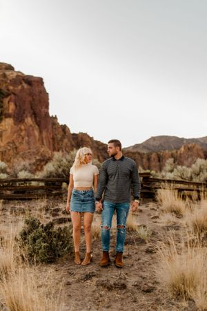 Couple standing together against dramatic red rock formations in desert landscape.