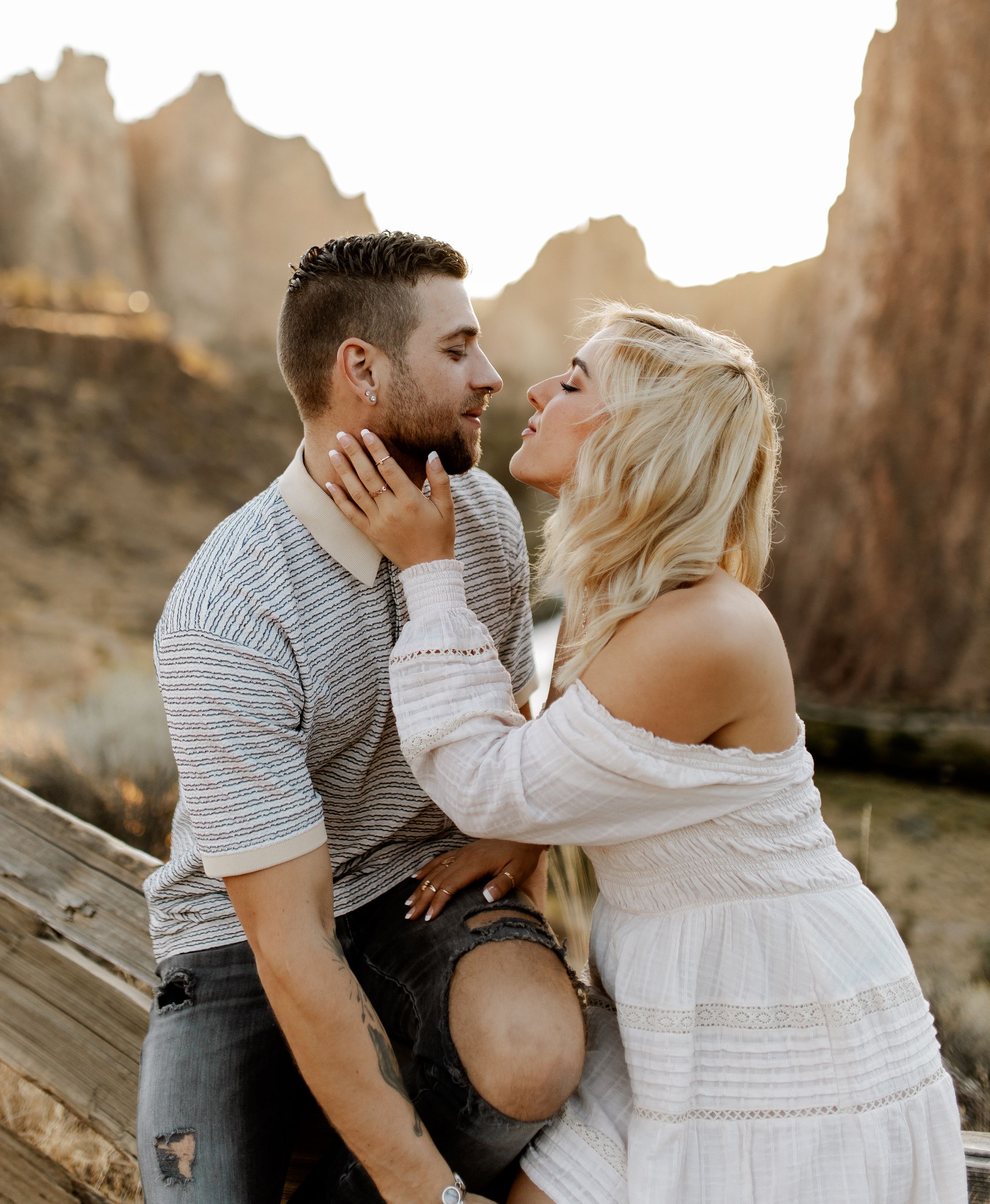 Romantic desert engagement photo on wooden fence at sunset.
