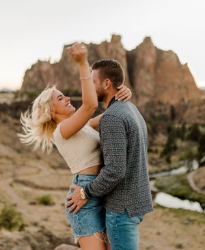 Romantic couple embracing against backdrop of dramatic red rock formations in desert landscape.
