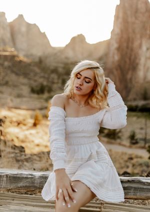 Woman in white dress poses on wooden fence with desert cliffs in background.