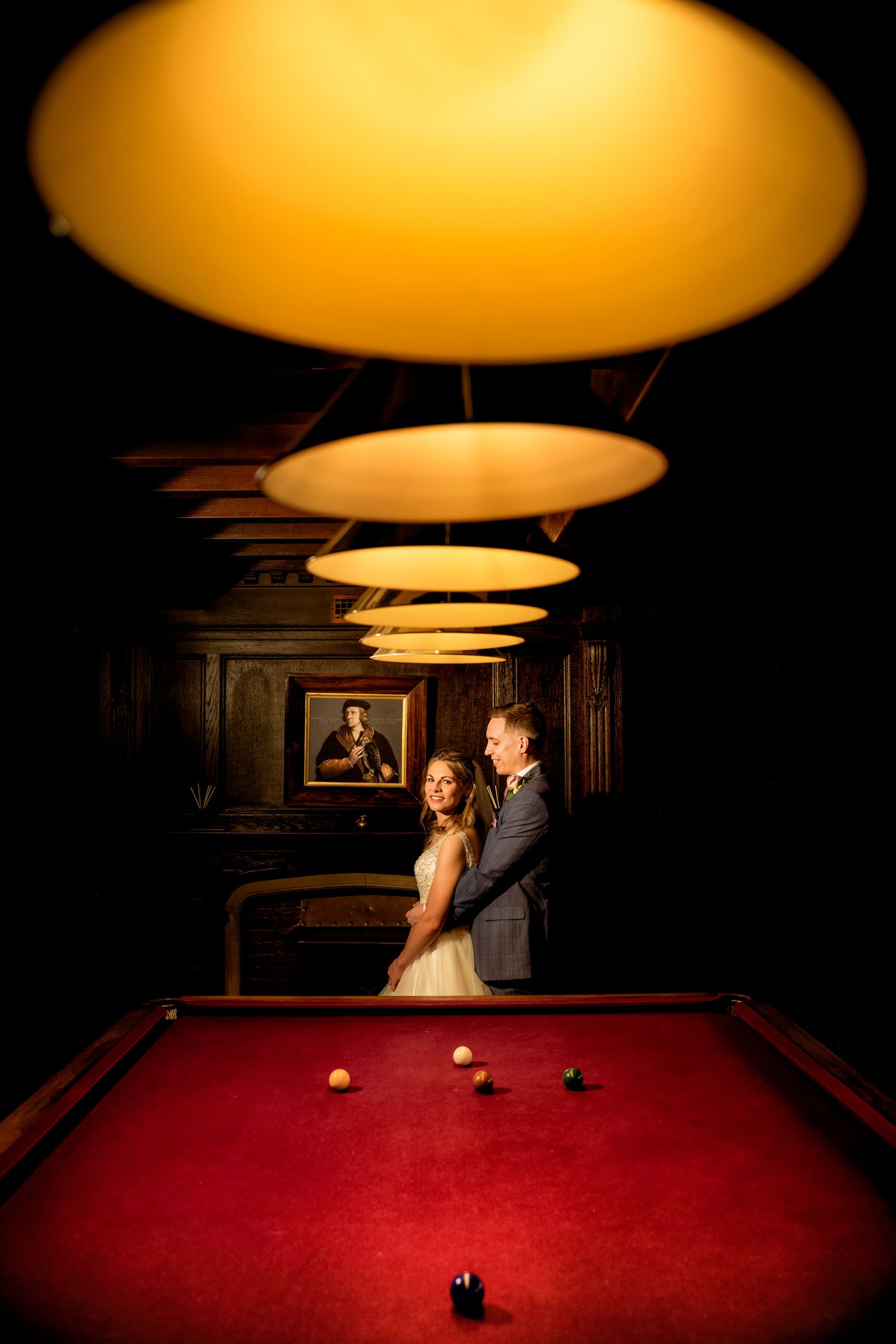 Dramatic lighting over a red pool table creates moody ambiance in a wood-paneled billiards room.