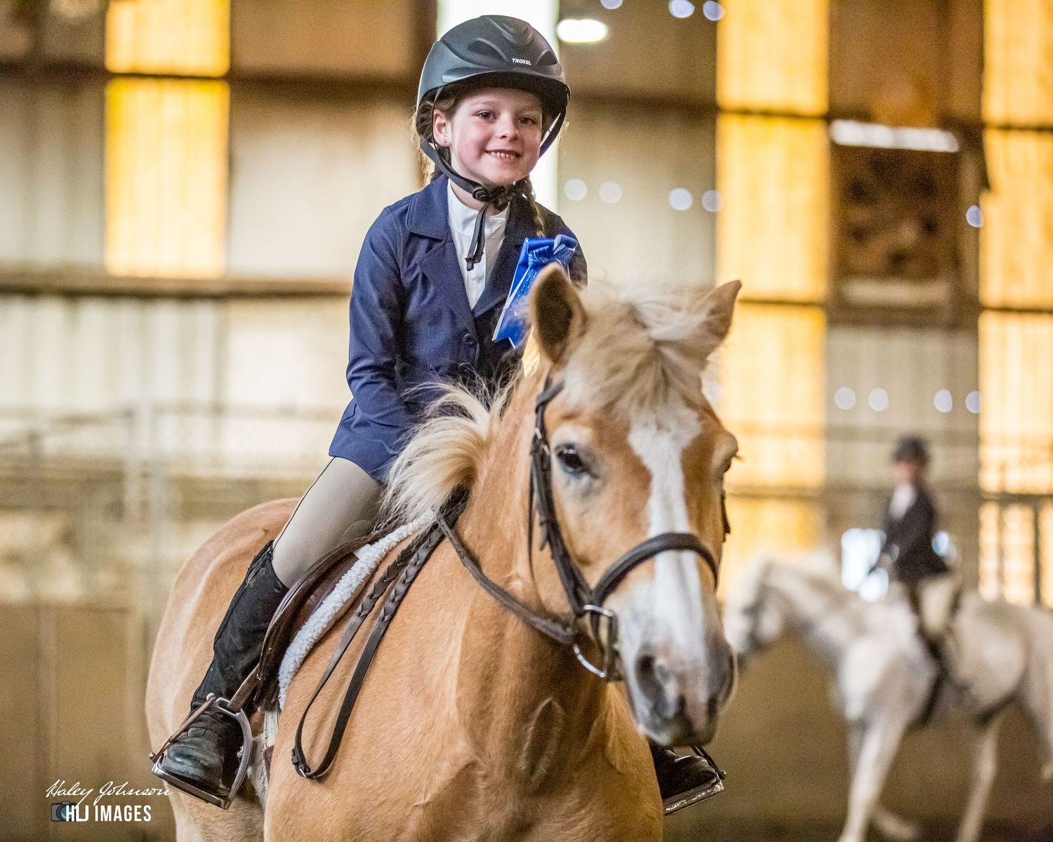 Young equestrian aboard a chestnut pony in an indoor riding arena.