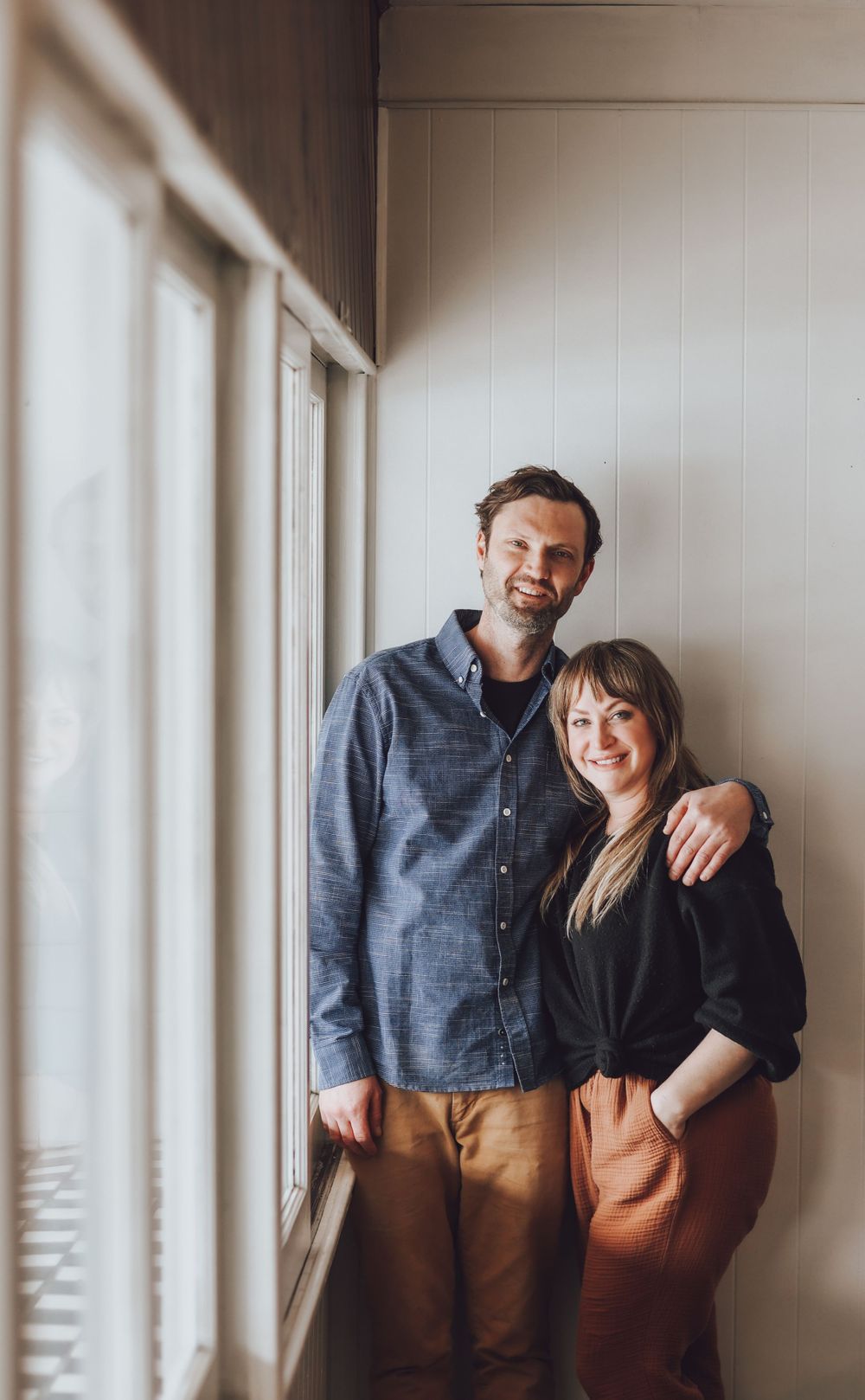 Couple posing together against white wall in casual outfits.