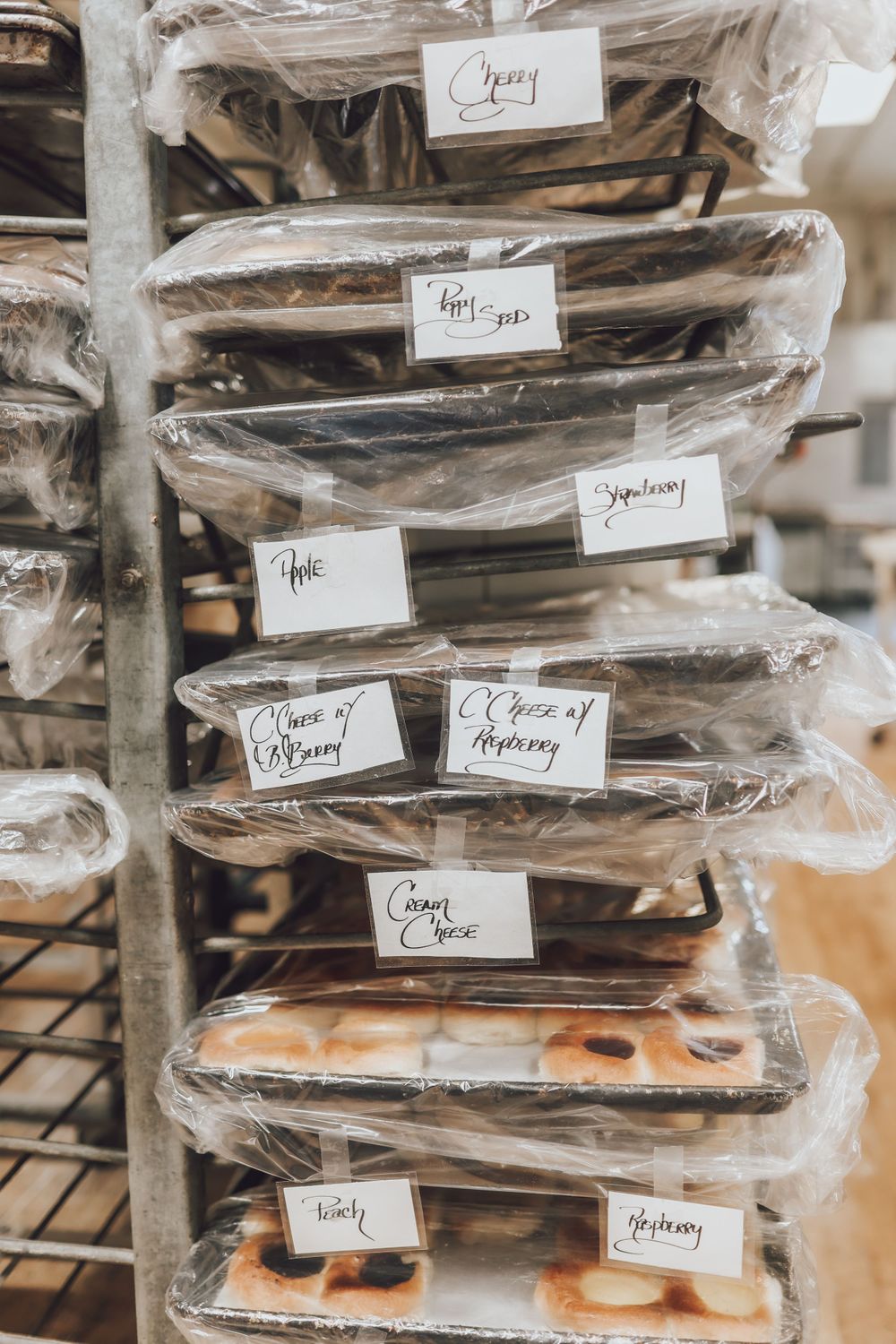 Stacks of wrapped baked goods with handwritten labels on bakery shelves.