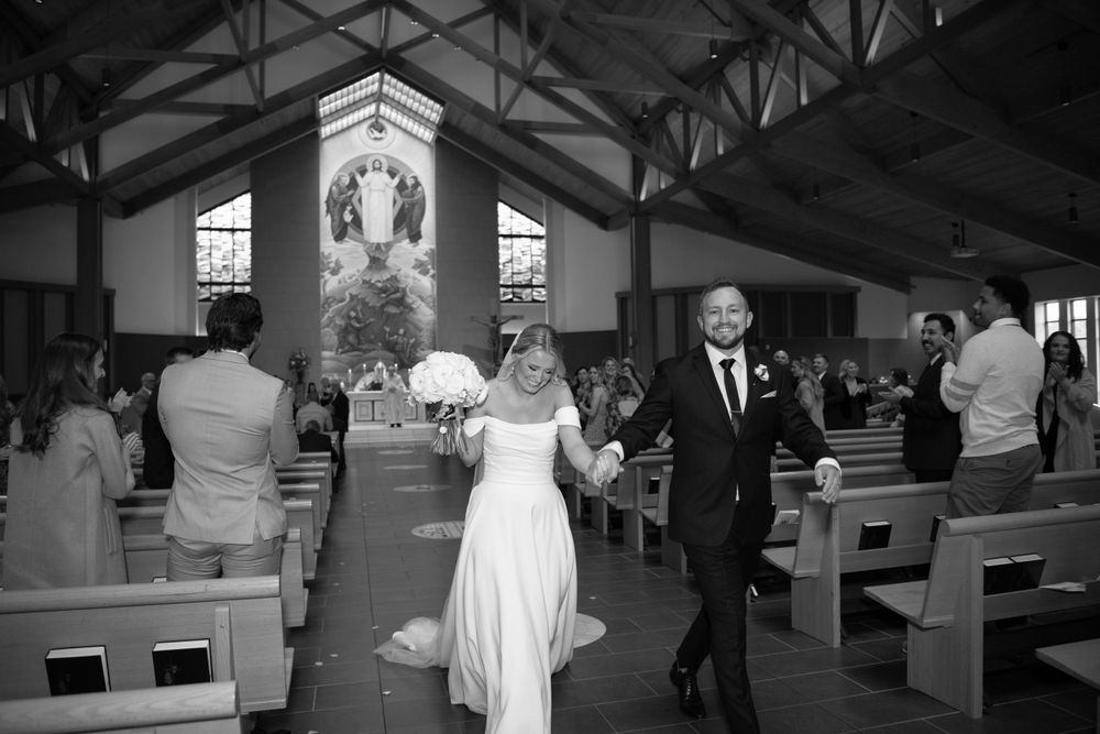 Wedding ceremony moment captured in black and white as couple exits traditional church aisle.