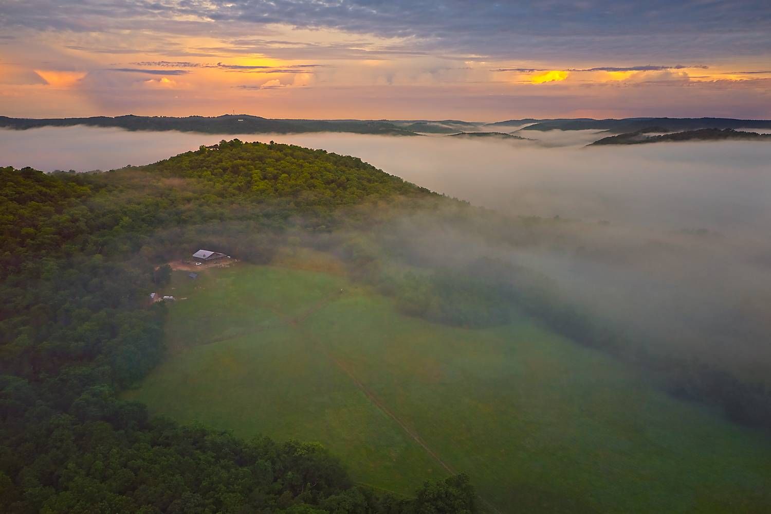 A farm in Eureka Springs, Arkansas, is partly obscured by a thick blanket of fog as sunrise warms the nearby valleys.